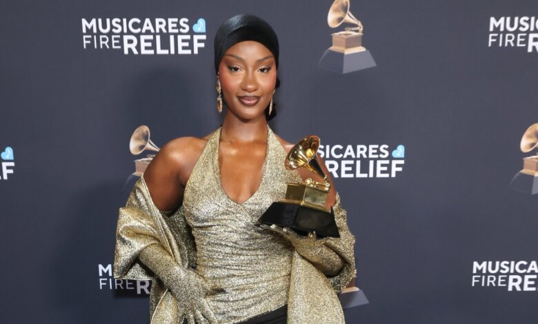 Nigerian singer Tems holding her Grammy award while posing at the MusiCares Fire Relief event in a gold outfit.